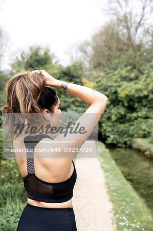 Young female runner tying hair into ponytail on riverside path