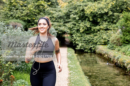 Young female runner listening to earphones while running on riverside path