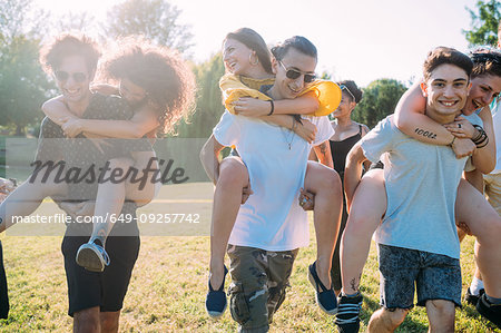 Group of friends piggyback racing in park