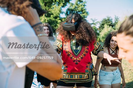 Group of friends watching woman looking into VR headset in park