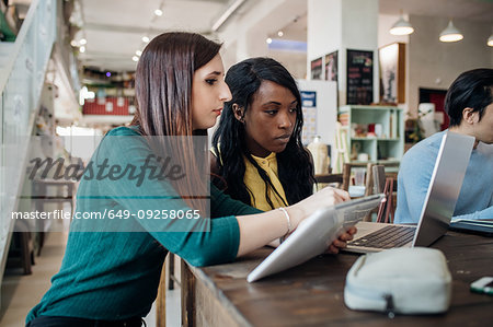 Two young businesswomen remote working, looking at laptop in cafe