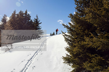 Mature male snowshoeing up snow covered mountain landscape, distant rear view, Styria, Tyrol, Austria