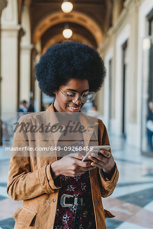 Young woman with afro hair using smartphone in building corridor