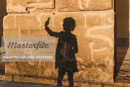 Shadow of woman taking selfie on stone wall