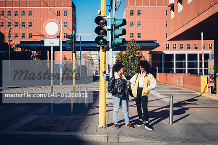 Two cool young female friends chatting at pedestrian crossing