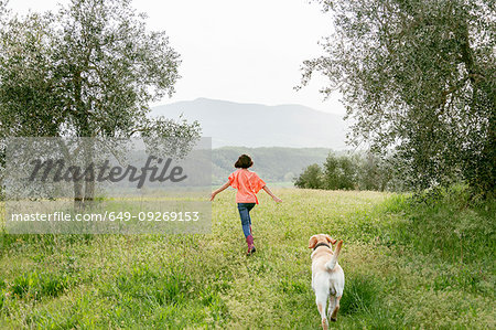 Girl running with labrador dog in scenic field landscape, rear view, Citta della Pieve, Umbria, Italy Girl running with labrador dog in scenic field landscape, rear view, Citta della Pieve, Umbria, Italy