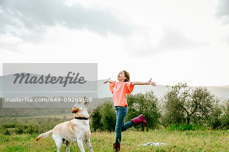 Girl with open arms playing with labrador dog in scenic field landscape, Citta della Pieve, Umbria, Italy Girl with open arms playing with labrador dog in scenic field landscape, Citta della Pieve, Umbria, Italy