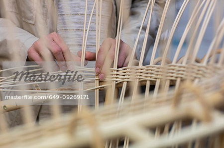 Young female basket maker weaving in workshop, mid section