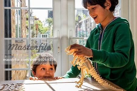 Boy and little brother playing with wooden dinosaur