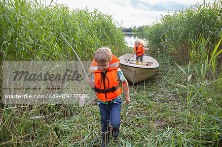 Brothers playing on boat moored in grass field