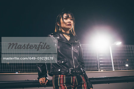 Woman leaning against railing, fencing and floodlights in background, Milan, Italy