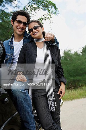 Young couple with motorbike smiling at camera