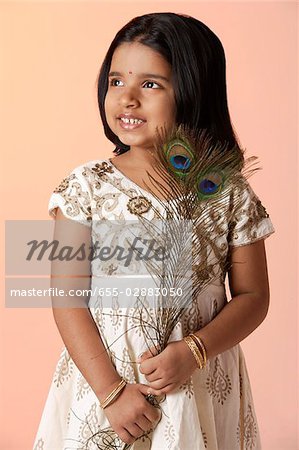 Little girl wearing traditional Indian clothing holding peacock feathers