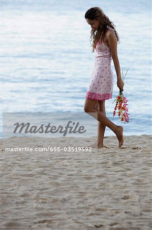 young woman walking on beach holding pink flowers