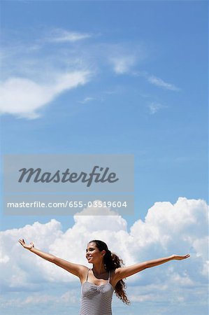 happy young woman raising her arms, blue sky and clouds background.