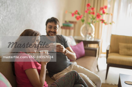Man and woman on sofa holding coffee cups smiling