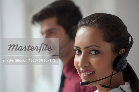 India, Young telemarketer looking at camera with her colleague in background