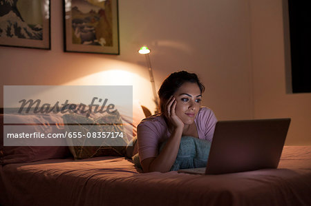 Singapore, Young woman relaxing with laptop on bed