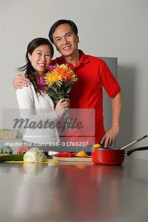 Mature couple in kitchen, embracing, woman holding bouquet of flowers