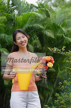Woman in garden, holding bouquet of flowers and watering can