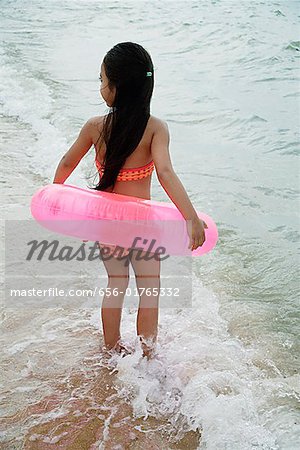 Young girl on beach wearing bikini and carrying pink inner tube