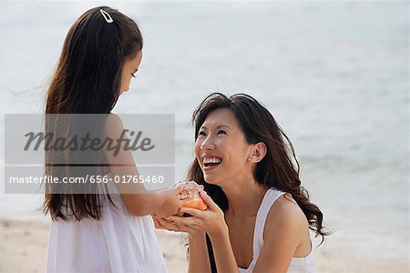 Mother and daughter on beach, daughter handing conk shell to mother, smiling