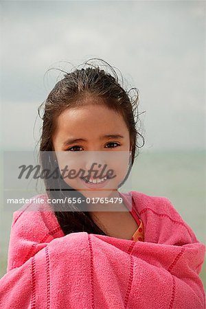 Young girl on beach wrapped in pink towel, smiling