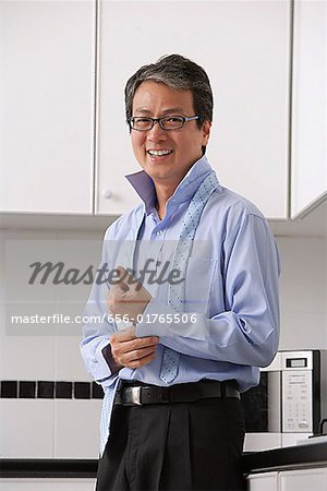 Man in kitchen, buttoning his shirt and tie loose around neck. smiling at camera.  Getting ready for work.