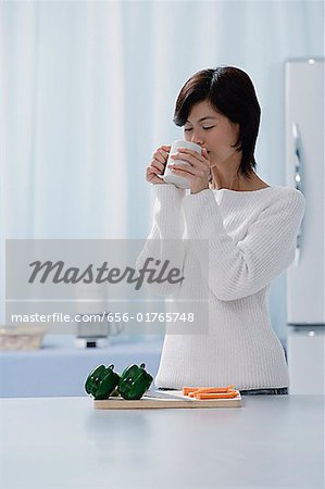Woman in kitchen, drinking from a cup