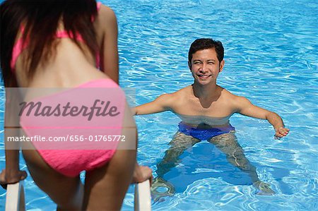 Man in swimming pool, smiling at woman standing in front of him