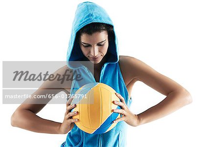 Woman holding volley ball, looking at ball, wearing hood, sports