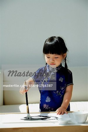 A small girl in blue silk cheongsam writing Chinese calligraphy