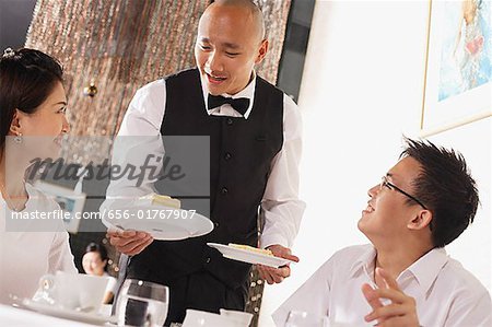 Waiter serving plates of dessert to customers in restaurant