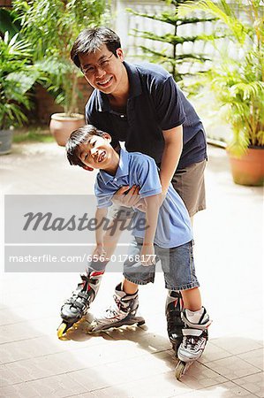 Father and son standing, wearing in-line skates, looking at camera
