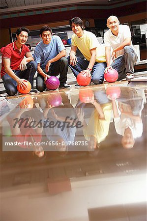 Four men in bowling alley, crouching, holding bowling balls