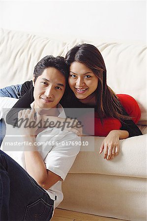 Couple in living room, woman lying in sofa, arm around man sitting in front of her