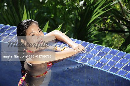 Woman leaning on edge of swimming pool, smiling at camera