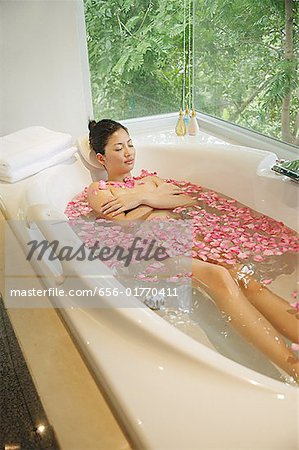 Woman taking a bath, flowers floating in water