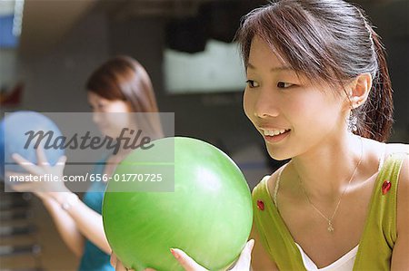 Two women holding bowling balls, preparing to bowl