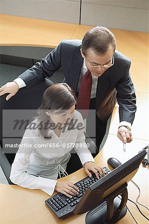 Executive working on computer, manager standing next to her, pointing at screen