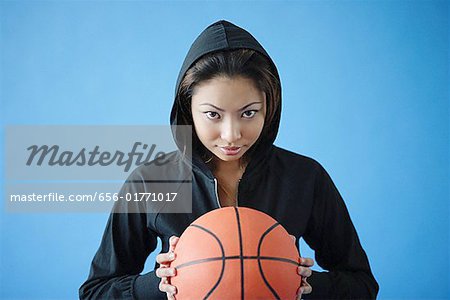 Woman wearing hooded shirt, holding basketball, looking at camera
