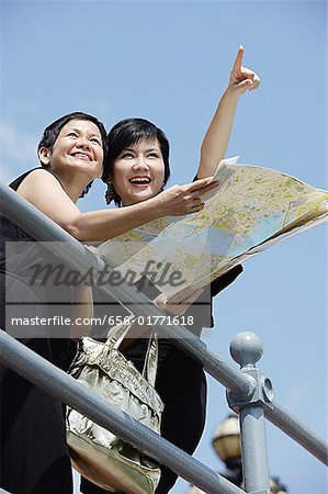 Two women side by side, one pointing in the distance, the other holding map