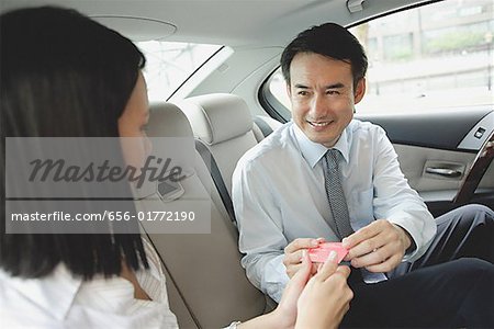 Businessman and businesswoman in backseat of car, exchanging business cards