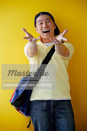 Man wearing cap and carrying satchel, reaching towards camera, smiling