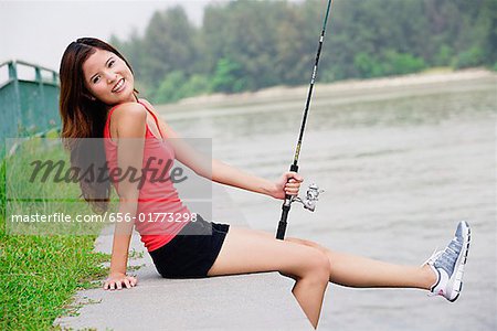 Woman sitting by river, holding fishing rod