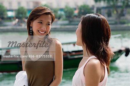 Two women smiling at each other, river behind them