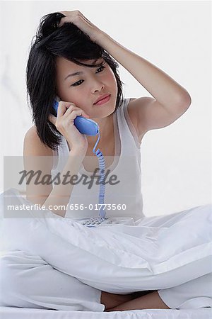 Young woman using telephone, hand on head