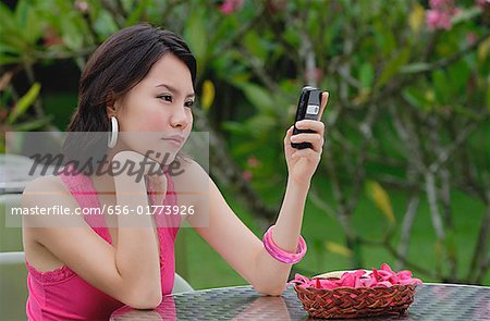 Young woman sitting at table outdoors, looking at mobile phone