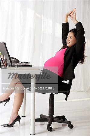Profile of pregnant businesswoman at desk stretching