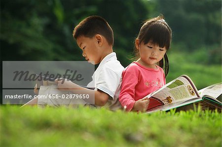 little boy and girl reading a book outdoors